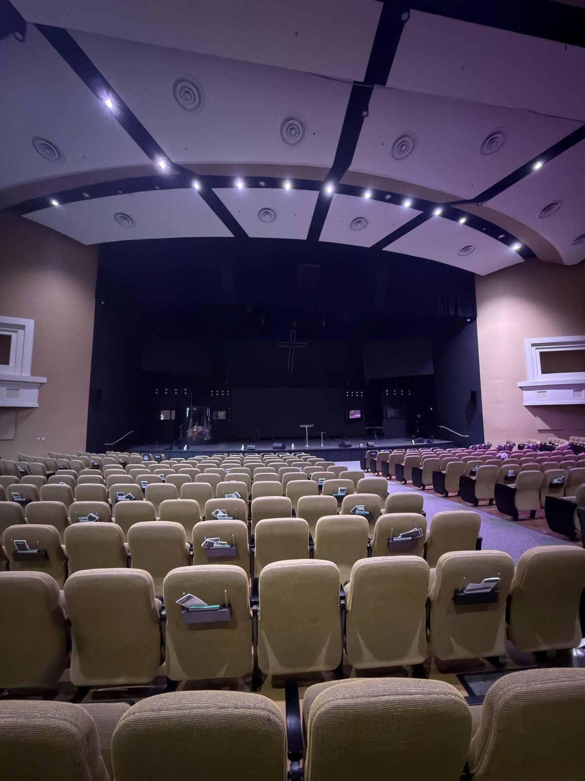 O auditório da Church In The Son visto do meio das poltronas, com o palco e a cruz ao fundo