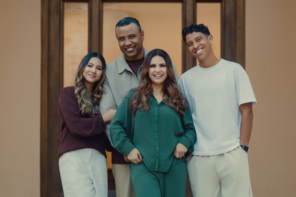 Pr. Gilmar Santos e Pra. Aline Barros com os filhos, Nicolas e Maria, sorrindo diante de uma porta de madeira